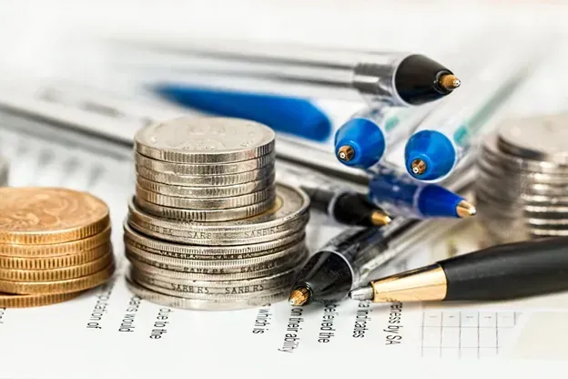 A pile of coins and pens on top of a piece of paper.