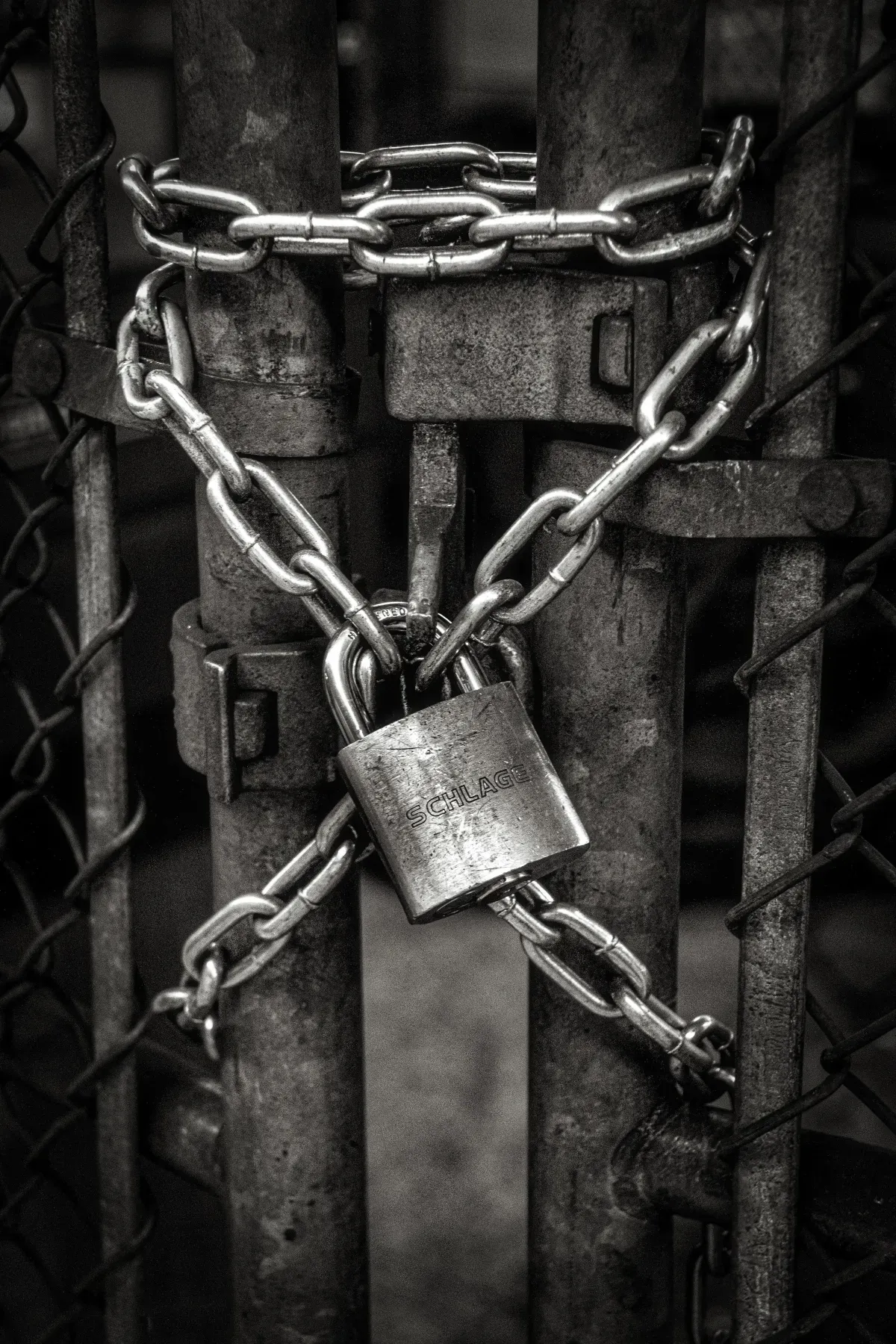 A black and white photo of a chain link fence with a padlock.