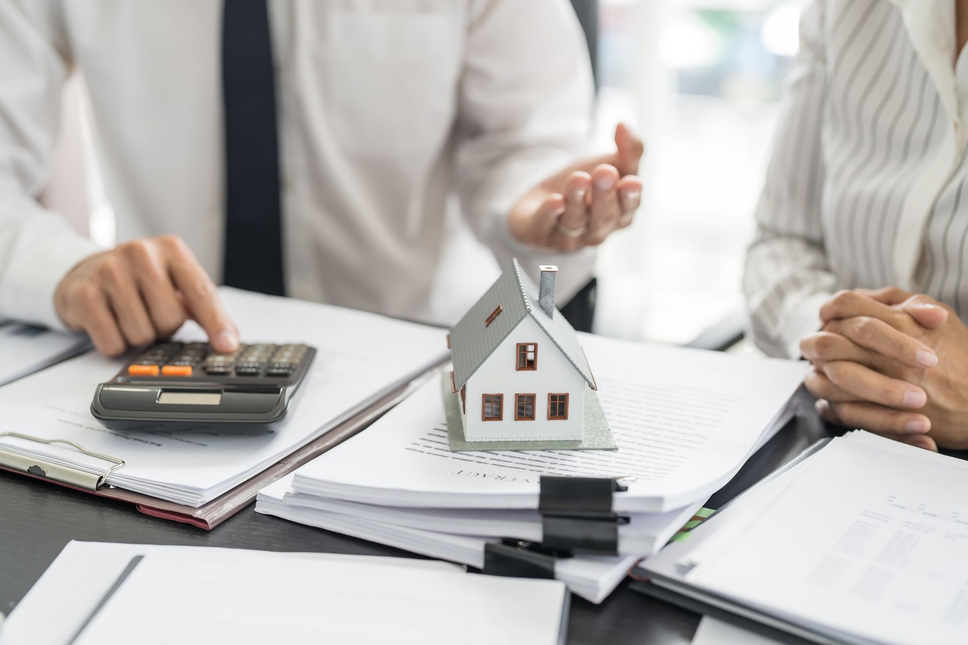 A man and a woman are sitting at a table with a model house and a calculator.