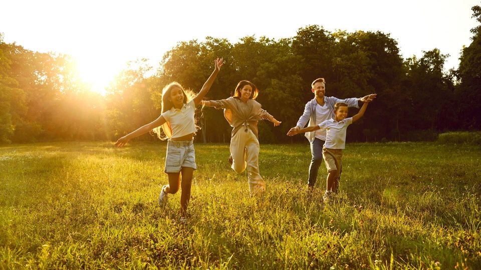 A family is running through a grassy field at sunset.