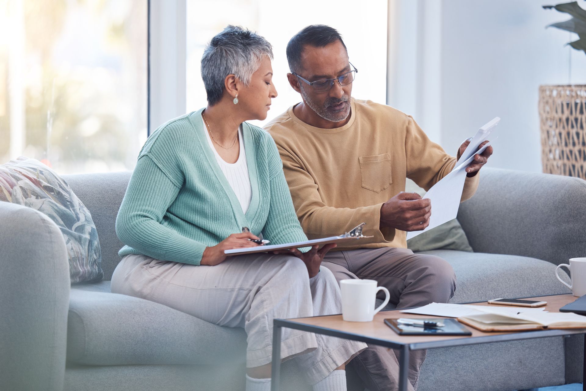 A man and a woman are sitting on a couch looking at a clipboard.