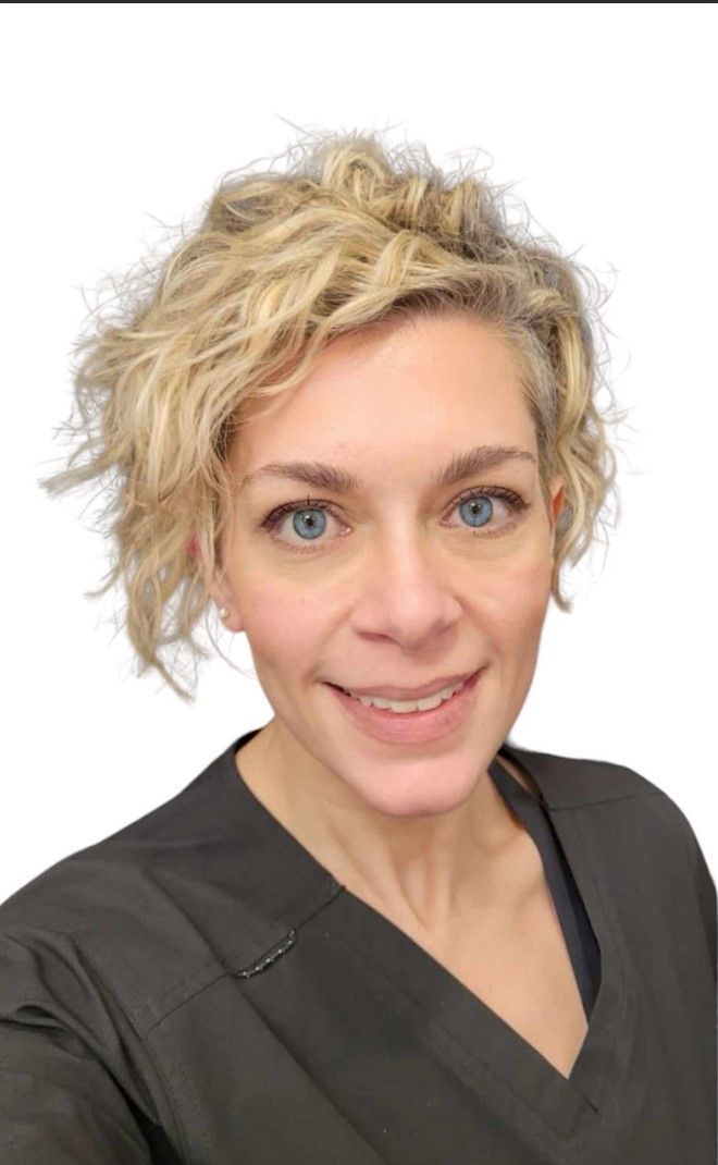 A woman in a black scrub top is smiling for the camera.