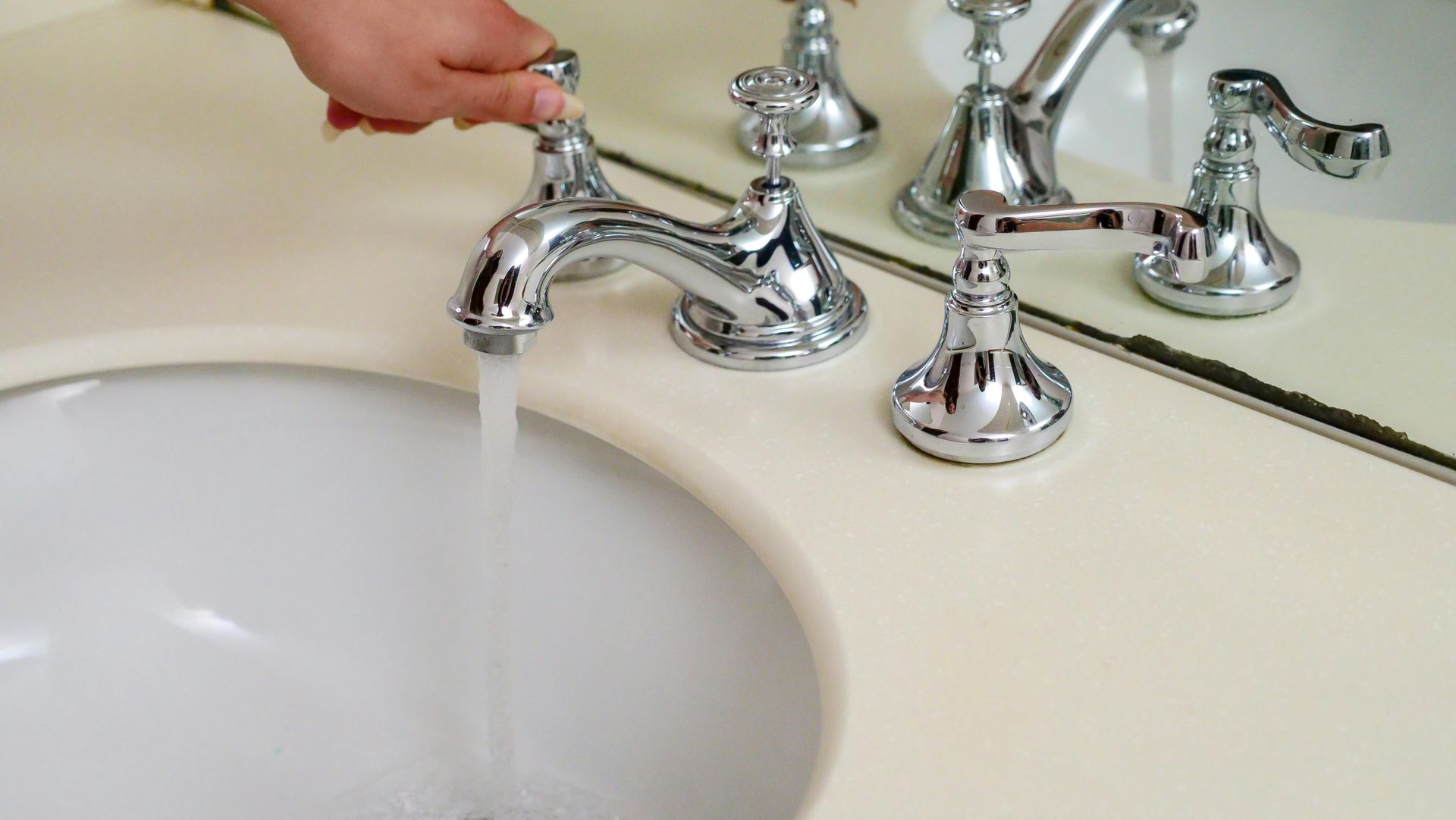 Un grifo de baño cromado girando a mano sobre un lavabo blanco.