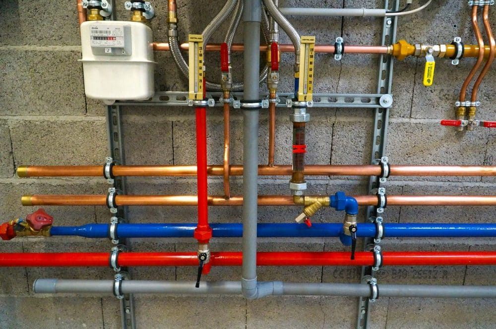 Tuberías y válvulas de servicios públicos en una pared, con líneas rojas, azules y de cobre y una caja de medidor blanca.