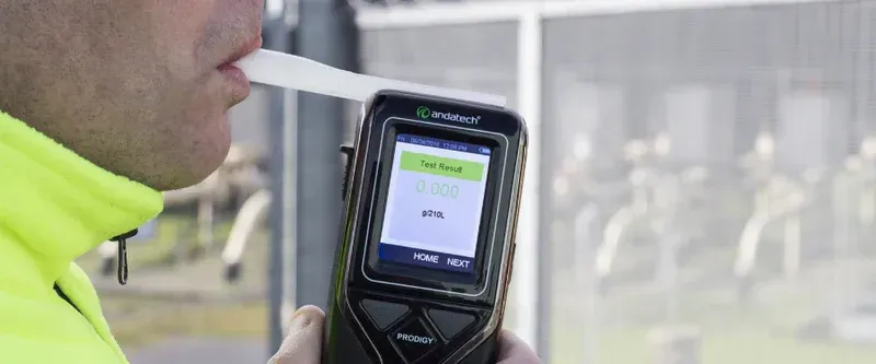 Person Blowing Into A Breathalyser. Device Screen Shows A Result. The Person Wears A Yellow Jacket — DAB Services in Cannonvale, QLD