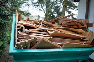 A dumpster filled with wood is sitting in front of a house.