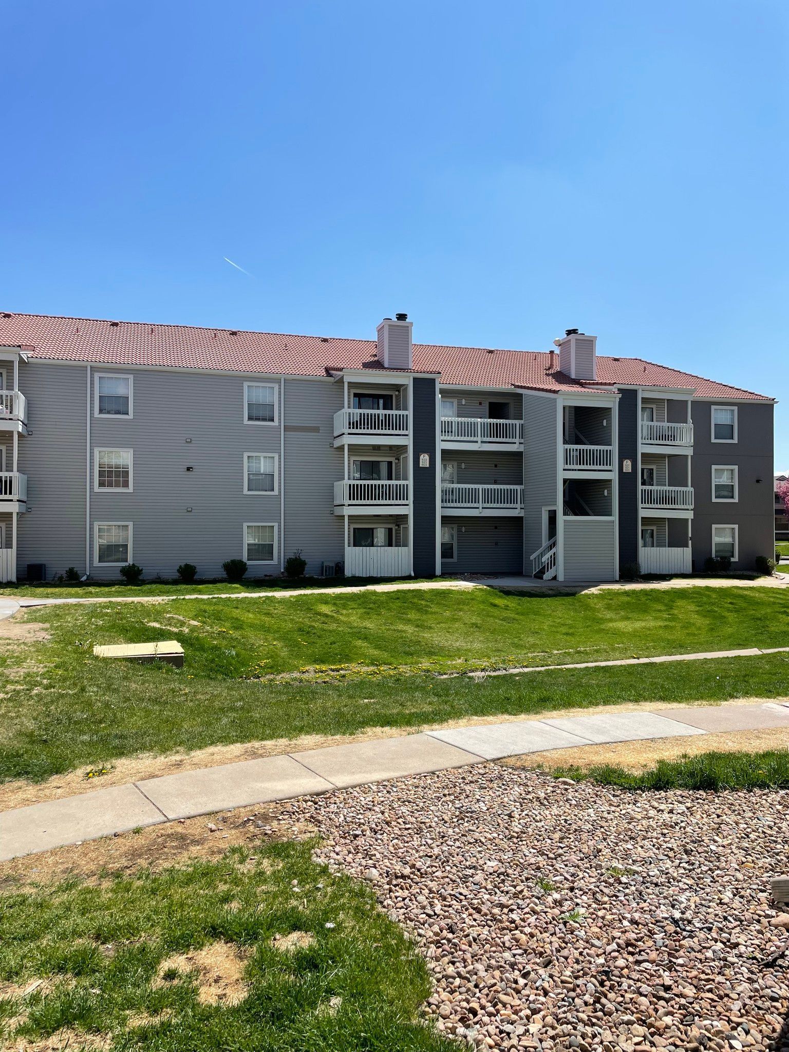 A large apartment building with a red roof is surrounded by grass and gravel.