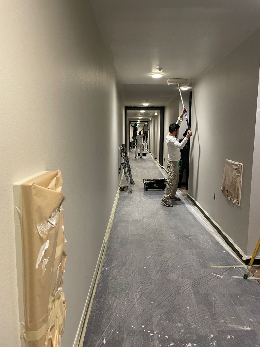 A man is painting a wall in a long hallway.