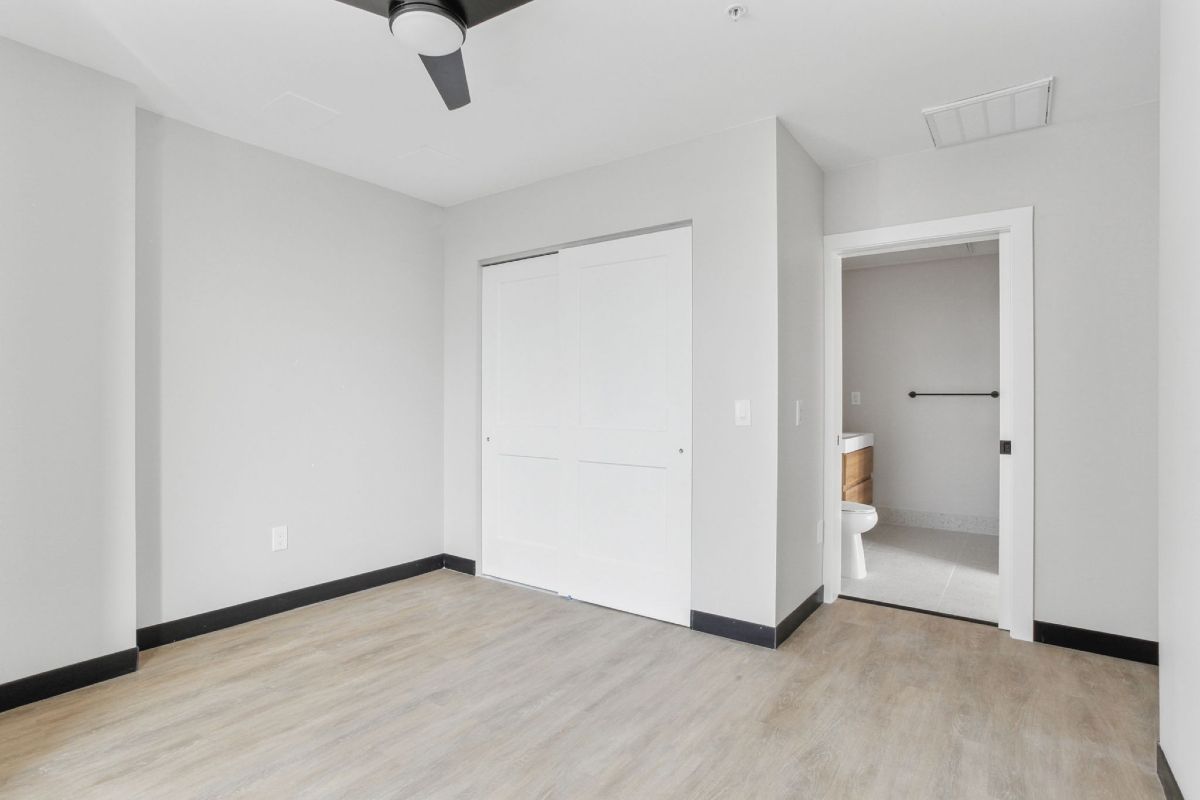 An empty bedroom with a ceiling fan and a toilet.