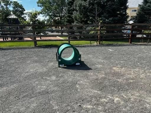 Dog agility tunnel on a gravel surface, with a wooden fence and trees in the background.