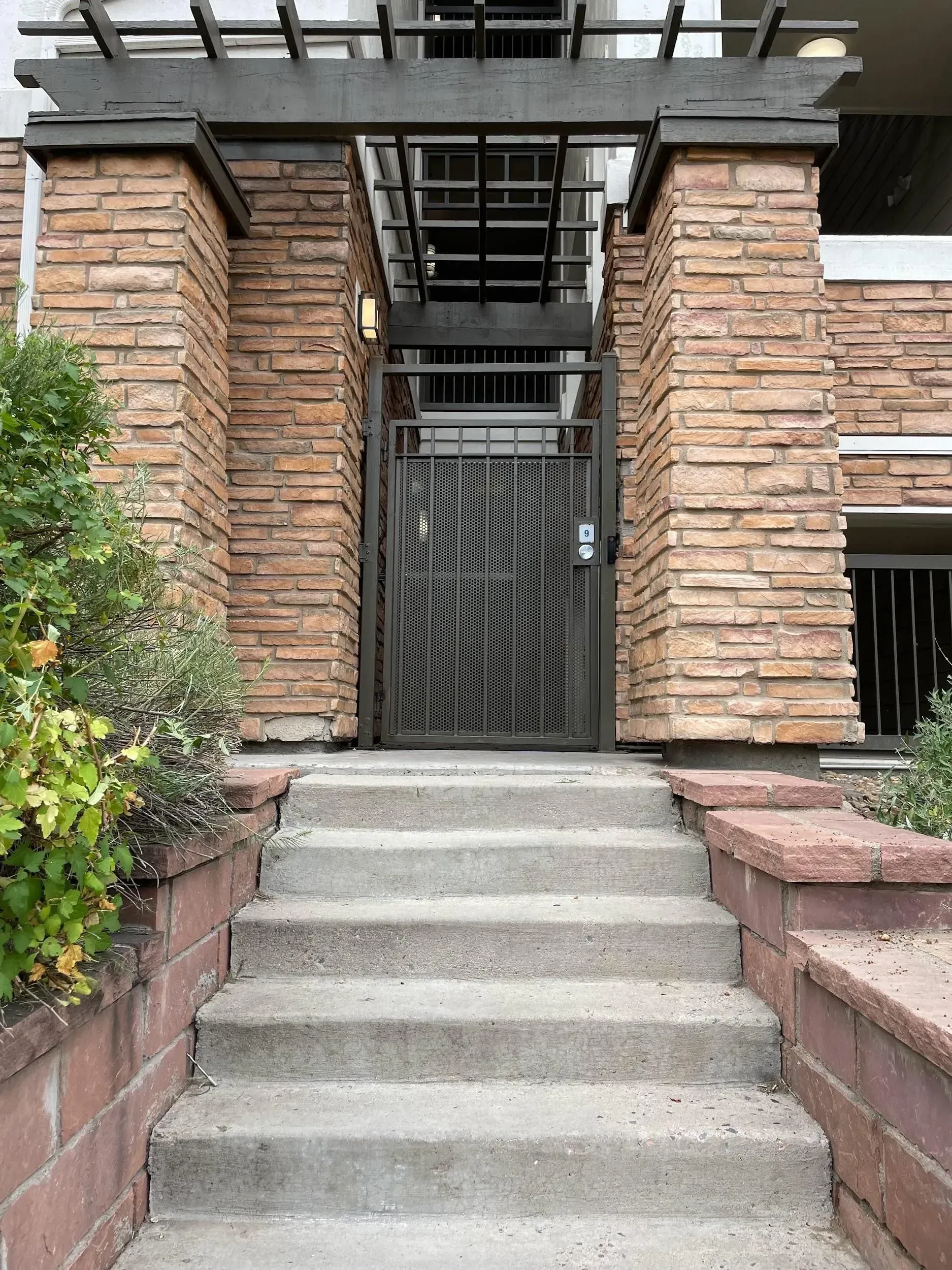 Steps leading up to a locked, ornate metal gate at a building entrance with brick columns.