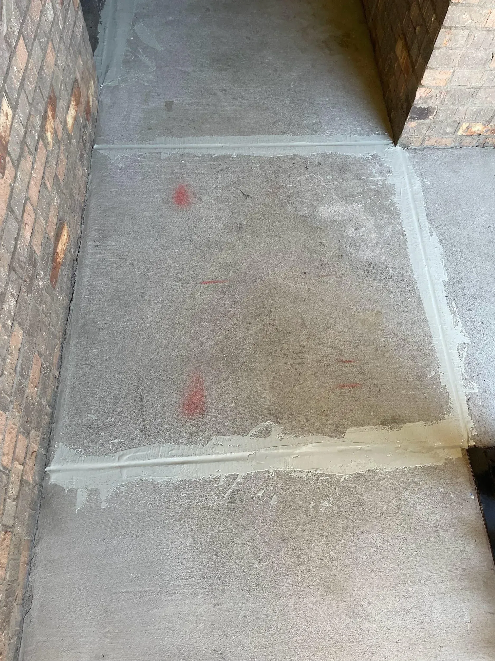 Concrete walkway with three large squares, sealed joints, and brick walls on either side.