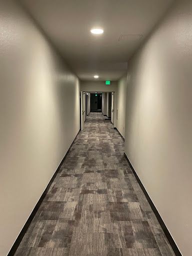 Long, narrow hallway with beige walls, carpet, and doors; exit sign visible at the end.