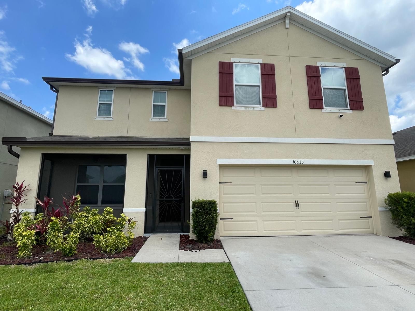 Two-story beige house with maroon shutters and a two-car garage under a blue sky.