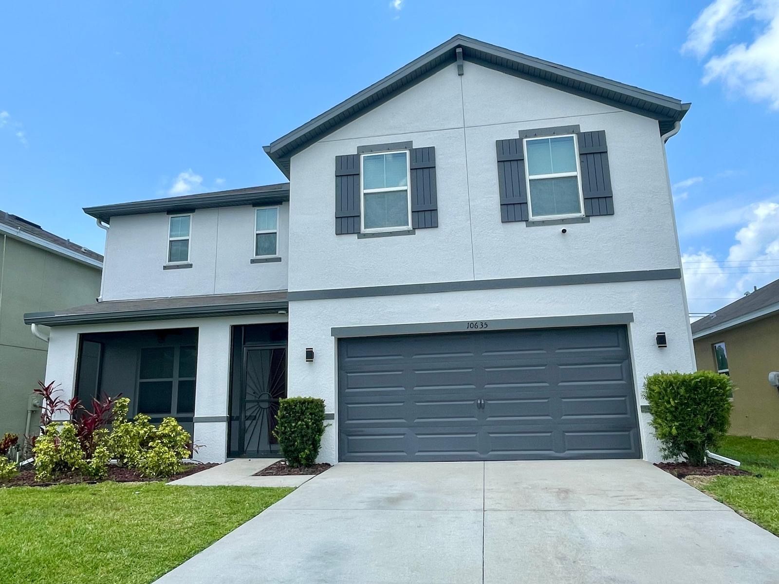 Two-story house with gray shutters and garage door, light blue sky.