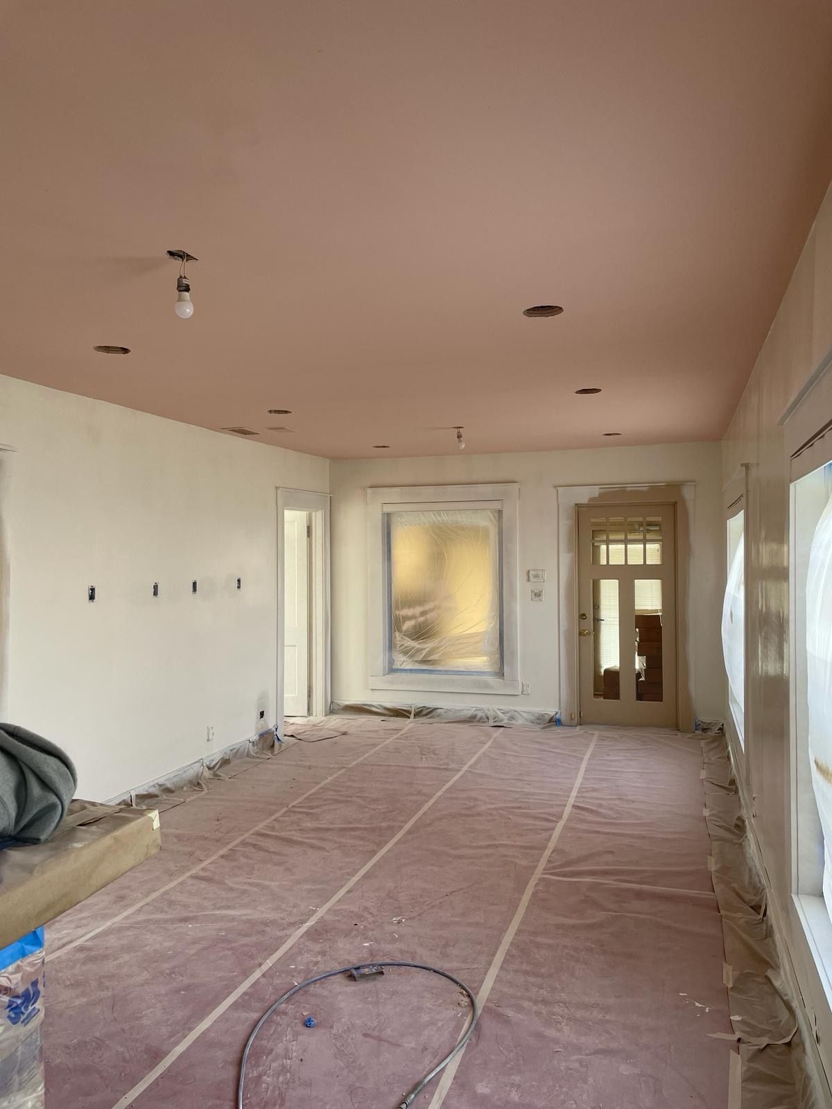 Room under renovation with pink ceiling and white walls, door, and windows. Covered floor.