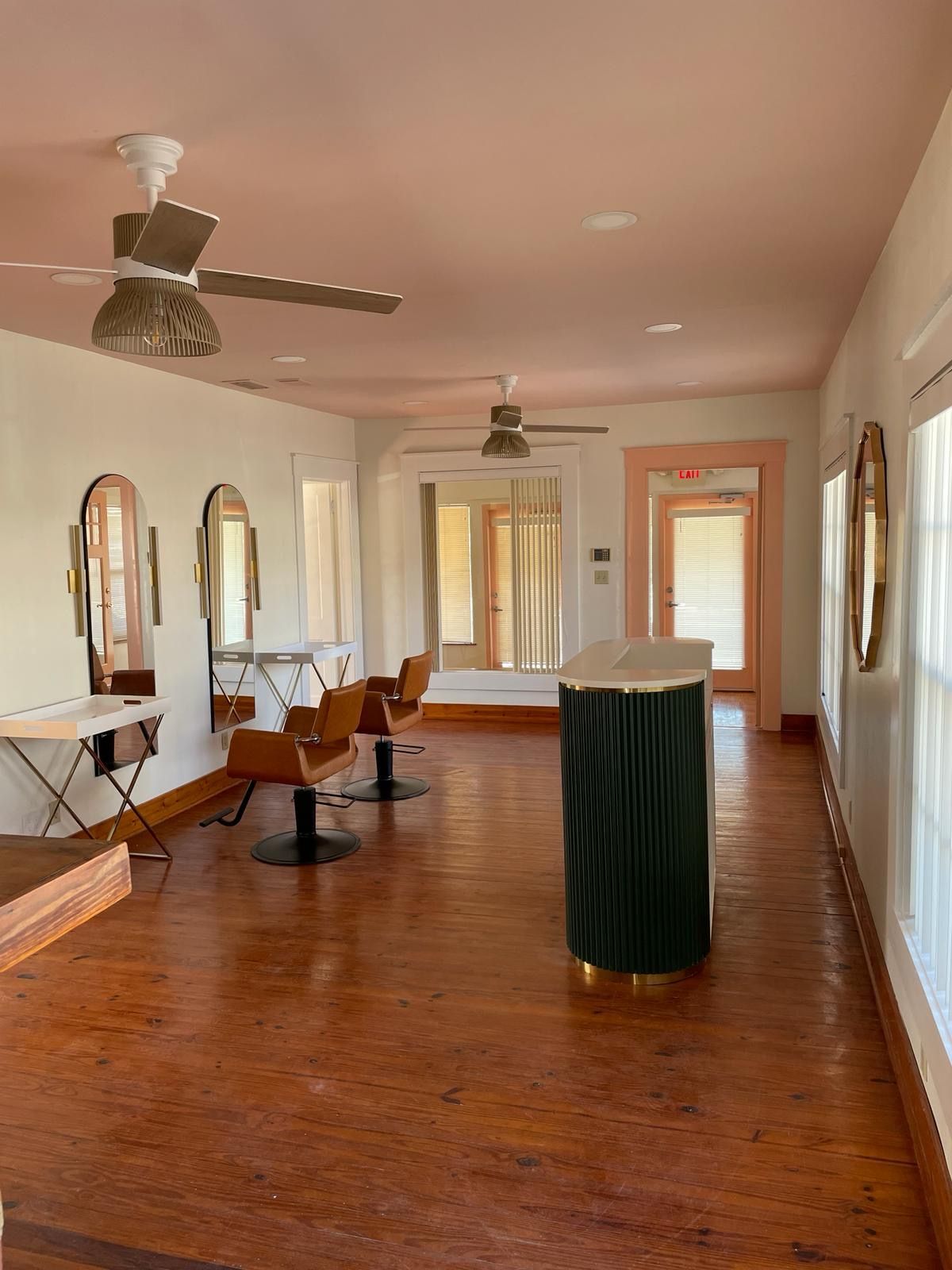 Hair salon interior with mirrors, chairs, and pink ceiling. Wooden floors and large windows.