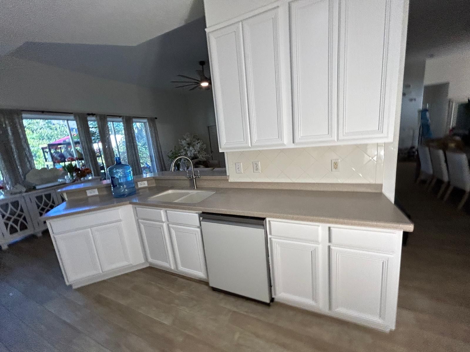 White kitchen cabinets with gray countertops and a dishwasher. Windows are in the background.