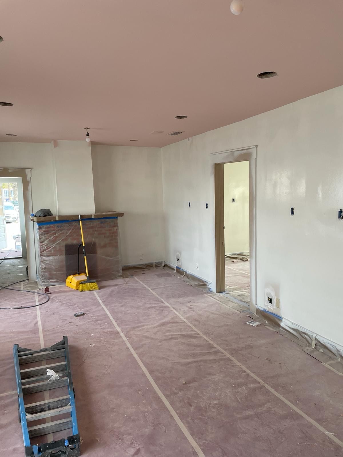 Room undergoing renovation, pink ceiling, white walls, exposed wiring, ladder on floor.
