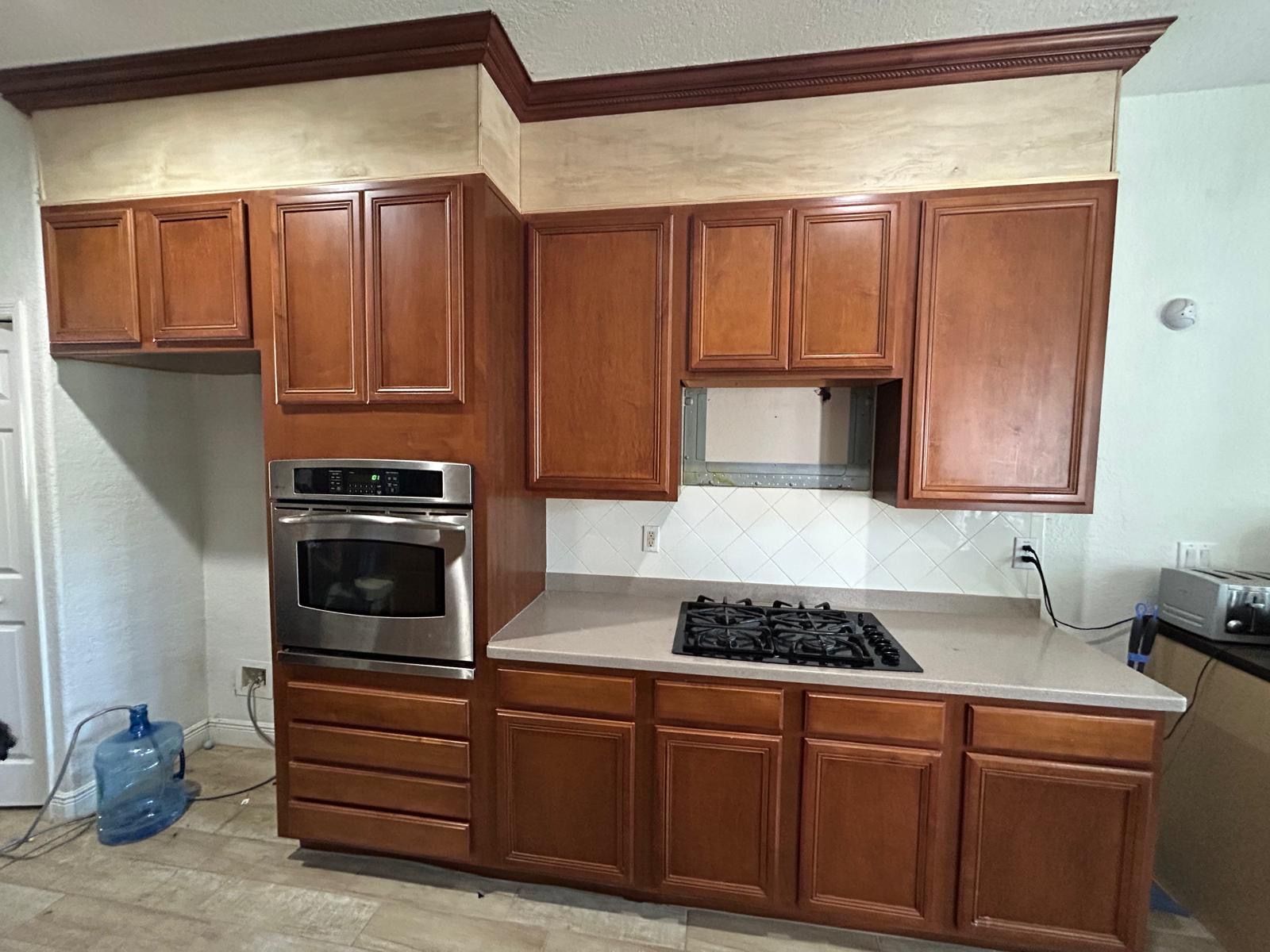 Kitchen cabinets in various sizes and a built-in oven and cooktop. Brown cabinets with a light countertop.