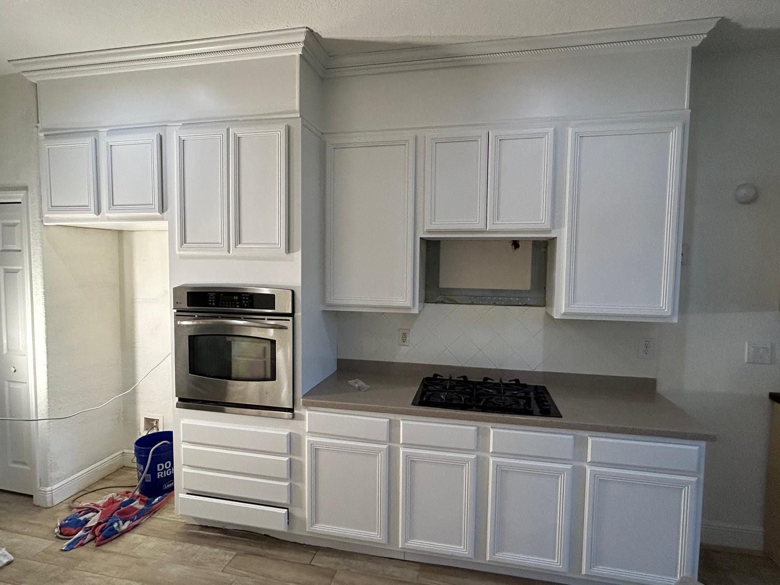 White kitchen cabinets with built-in oven, cooktop, and gray countertop.