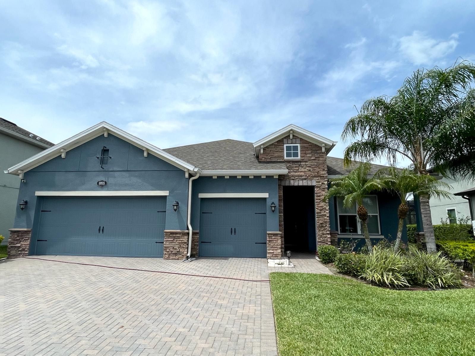 Blue house with two-car garage, stone accents, and a grassy yard under a cloudy sky.