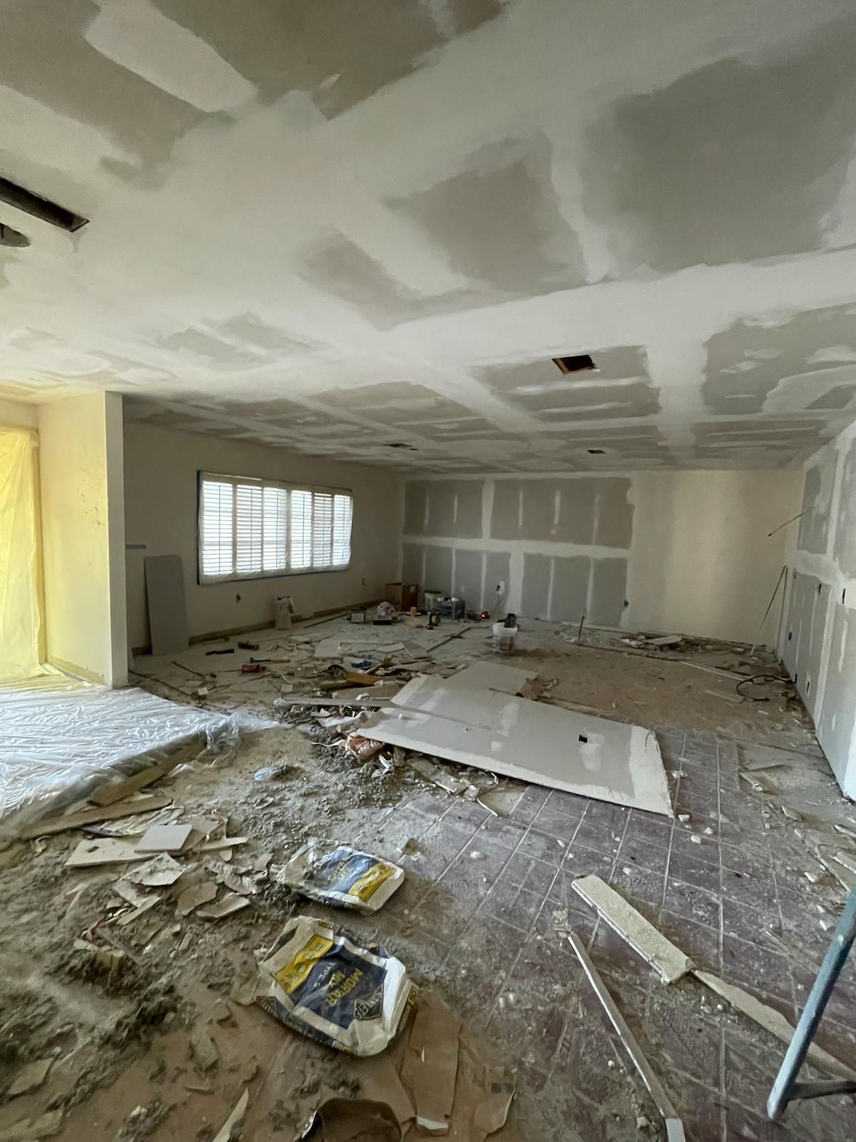 Room undergoing renovation, with drywall on walls and ceiling, debris on the floor, and a window.