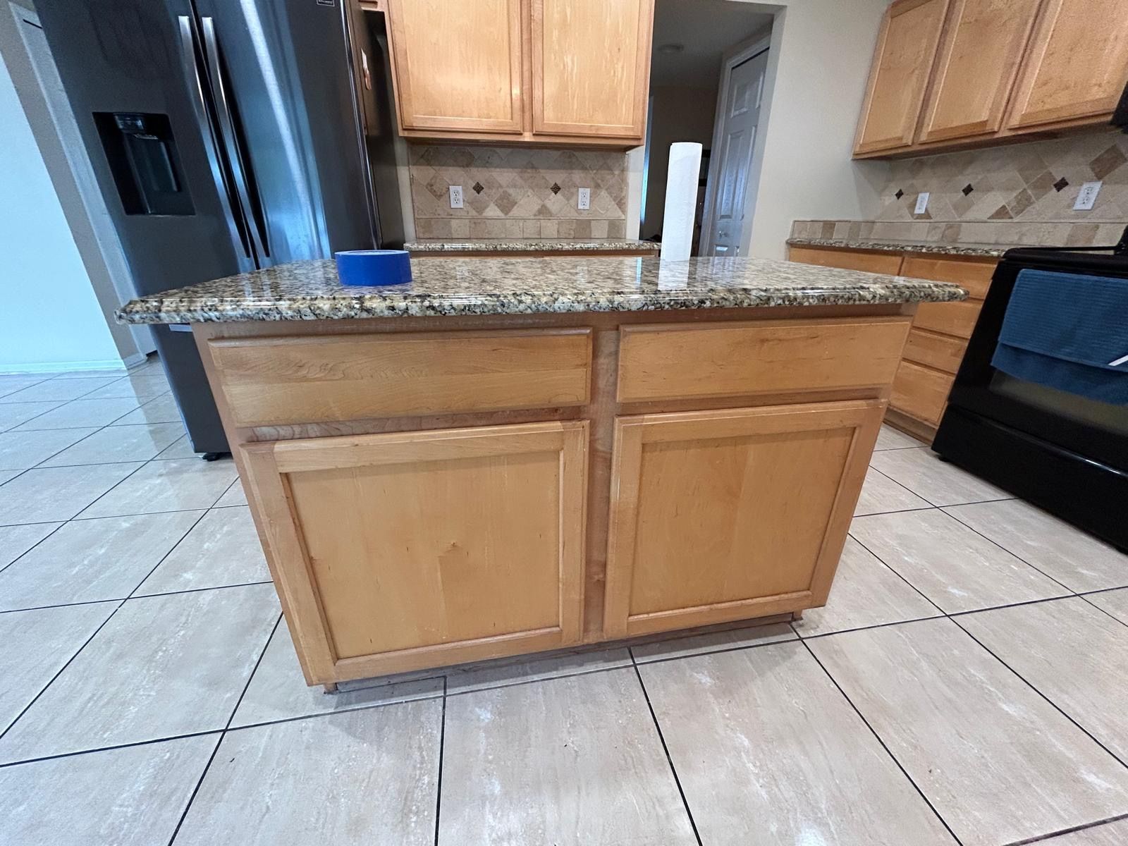 Kitchen with wooden cabinets, granite countertops, and tile flooring. Refrigerator and oven visible.