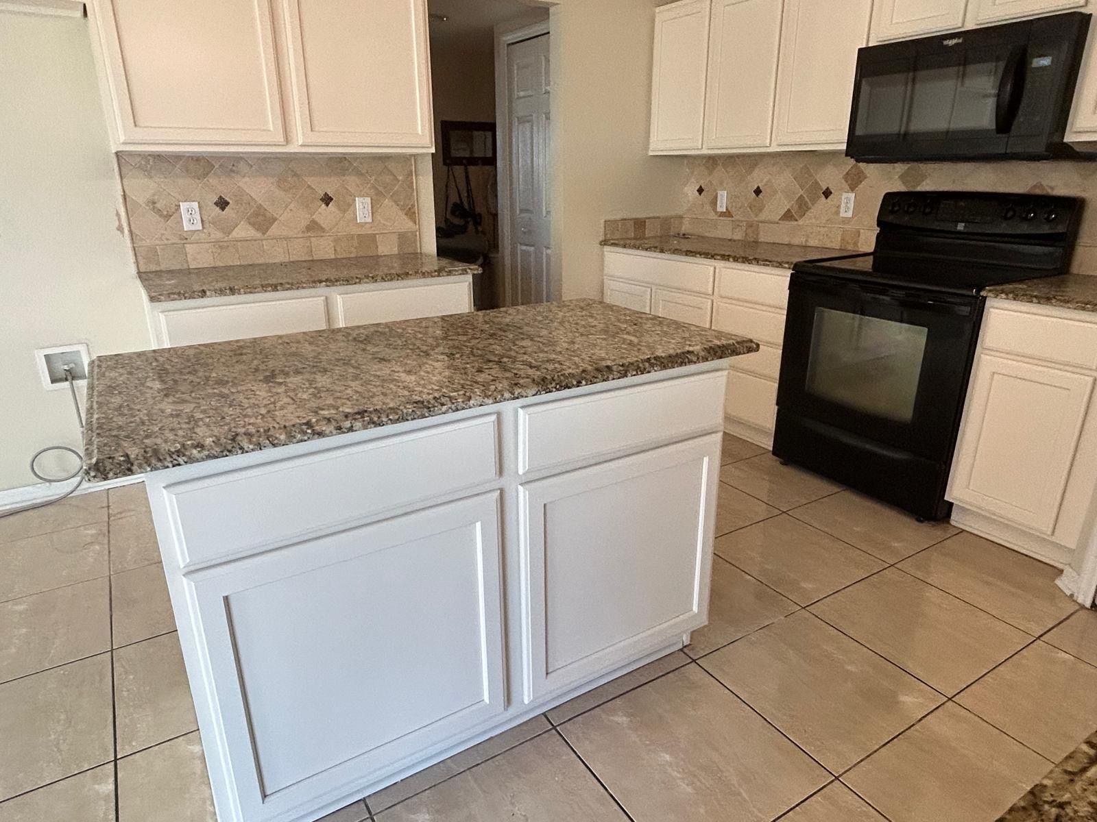 White kitchen with island, cabinets, granite countertops, and black appliances.