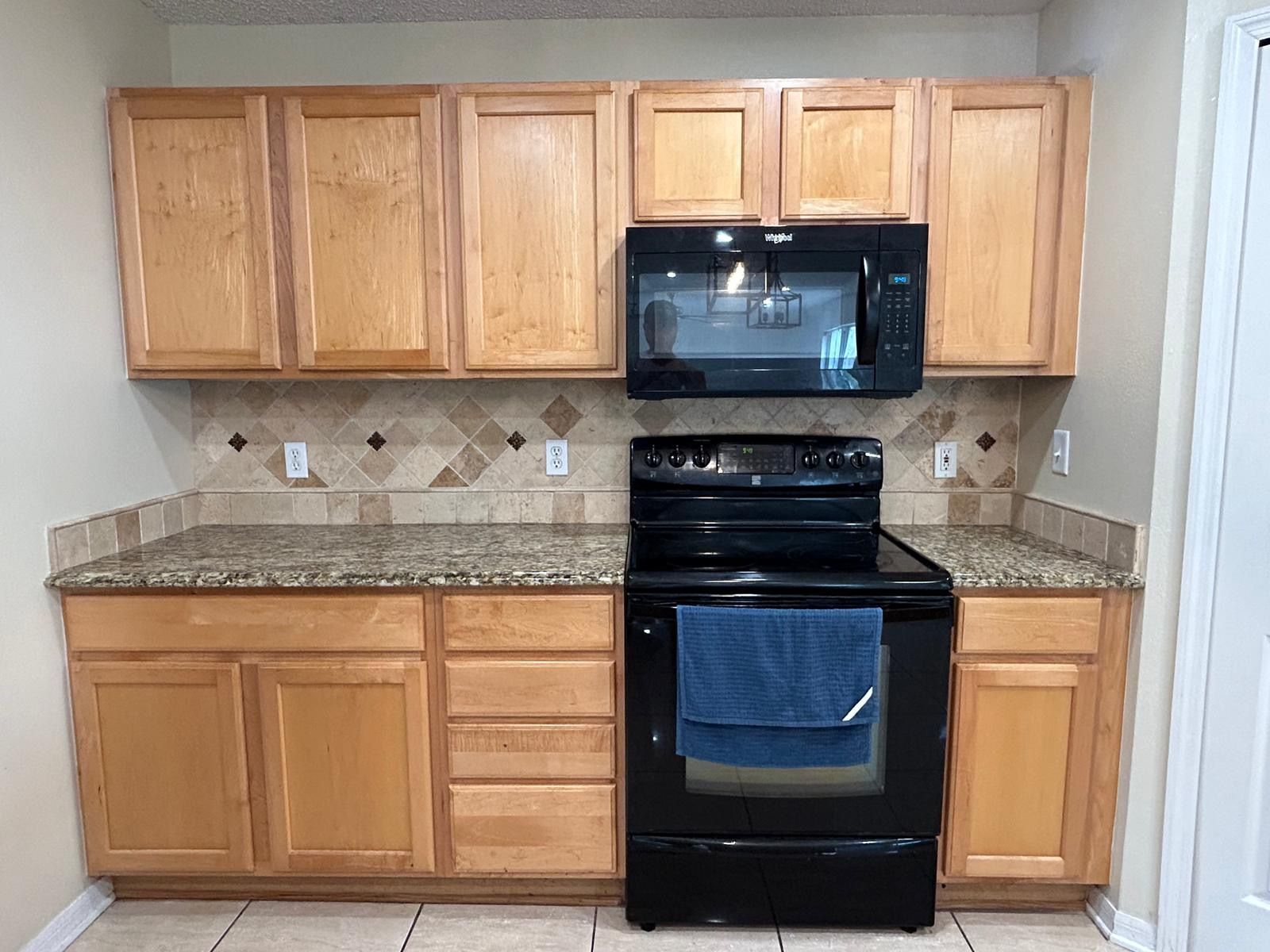 Kitchen with light wood cabinets, granite countertops, and black appliances.