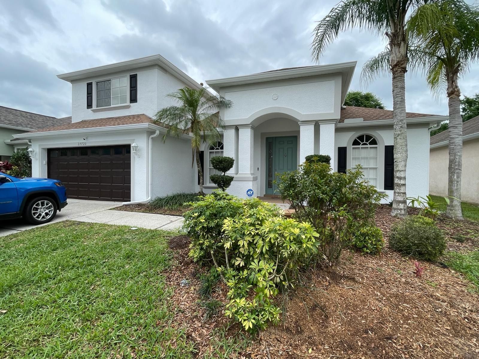 White two-story house with brown garage door, blue car in the driveway, and green lawn.