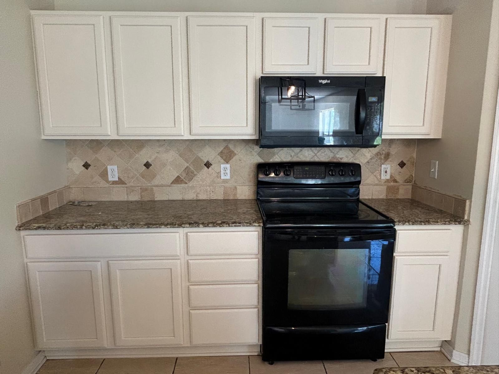 Kitchen with cream cabinets, black appliances, granite countertops, and decorative backsplash.