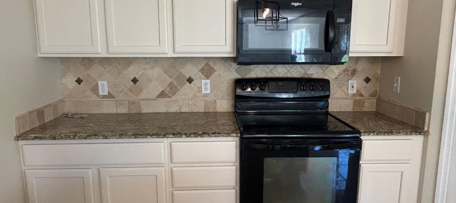 Kitchen with white cabinets, speckled countertop, tiled backsplash, and black appliances.