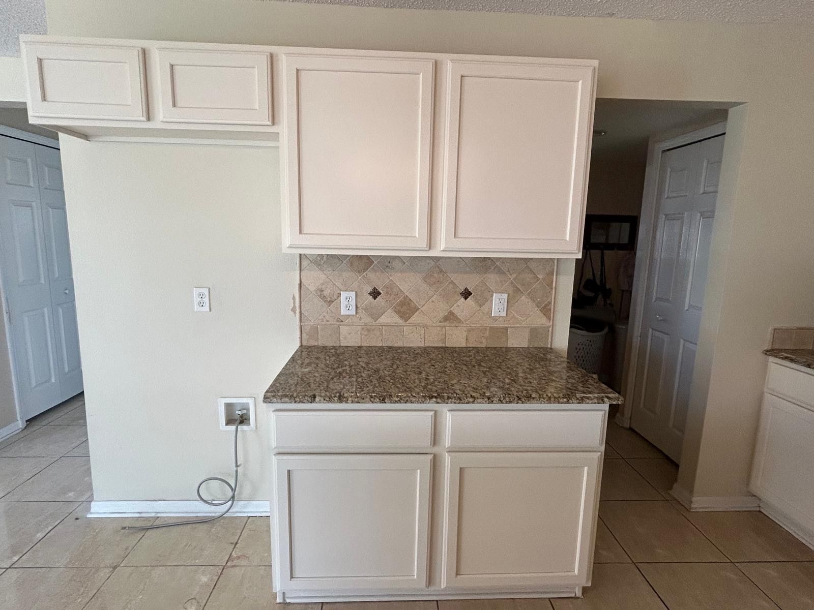 White kitchen cabinets with granite countertop and tiled backsplash.