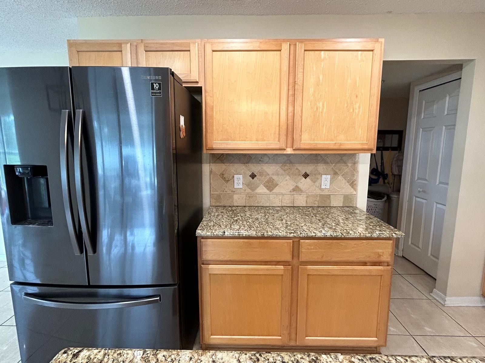Kitchen with wooden cabinets, a dark refrigerator, and a small countertop with tile backsplash.