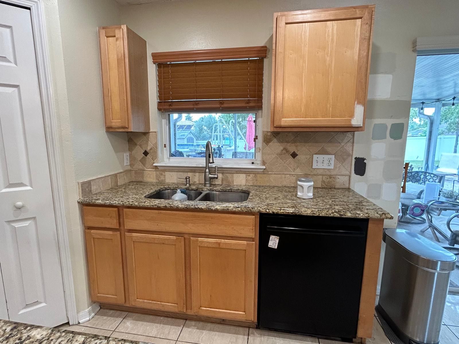 Kitchen with light wood cabinets, granite countertop, stainless steel sink, and black dishwasher.