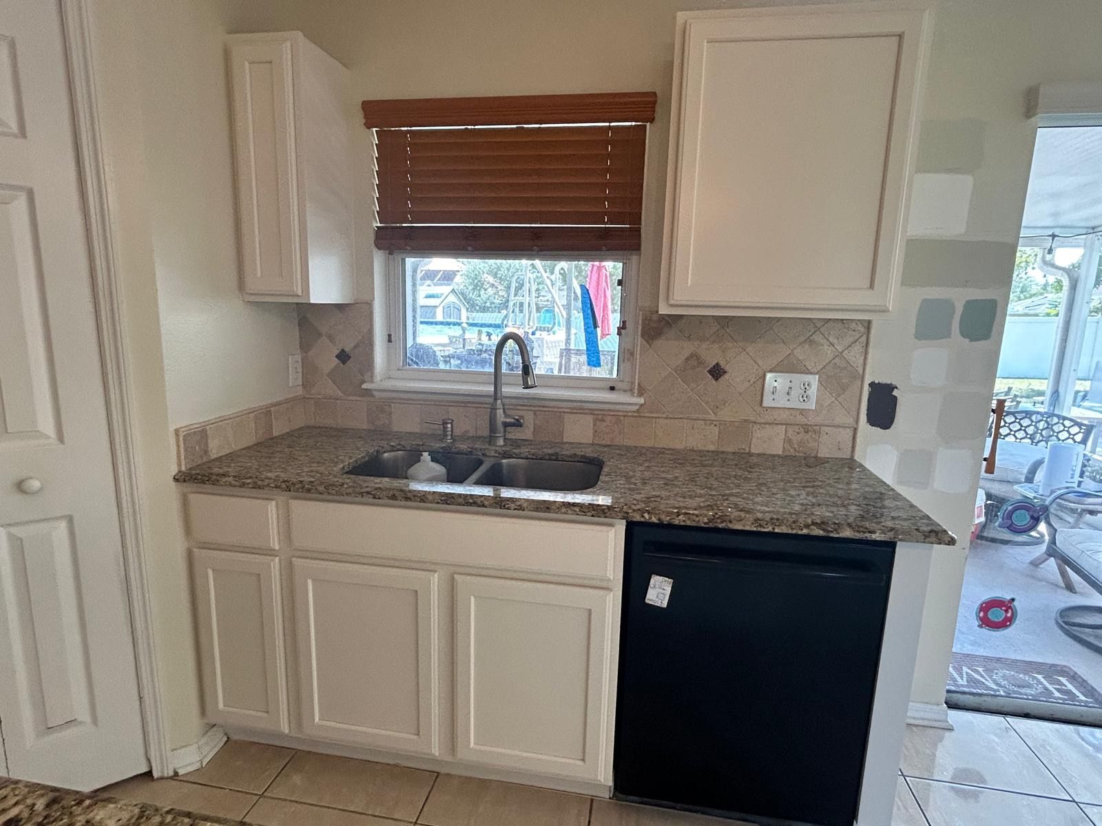 Kitchen with white cabinets, granite countertop, stainless steel sink, black dishwasher, and window with blinds.