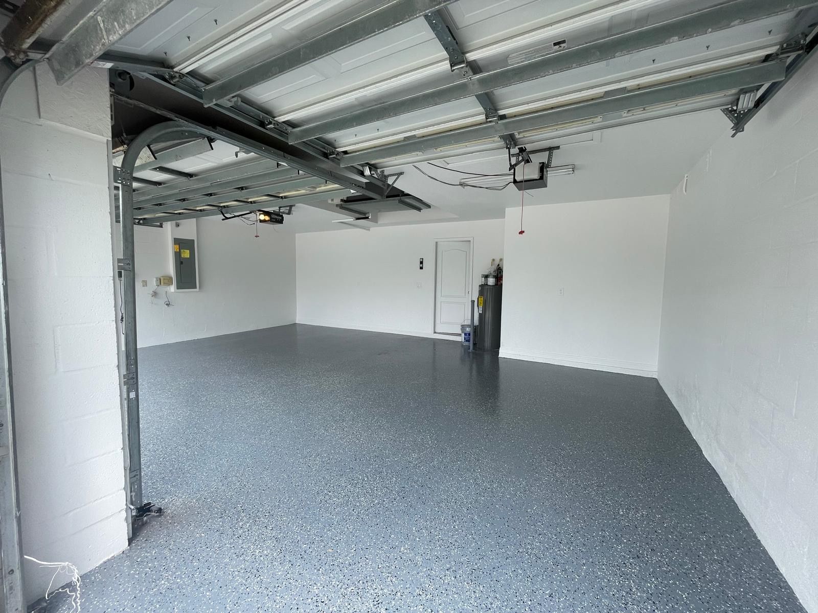 Empty garage with gray epoxy floor, white walls, and open garage door.