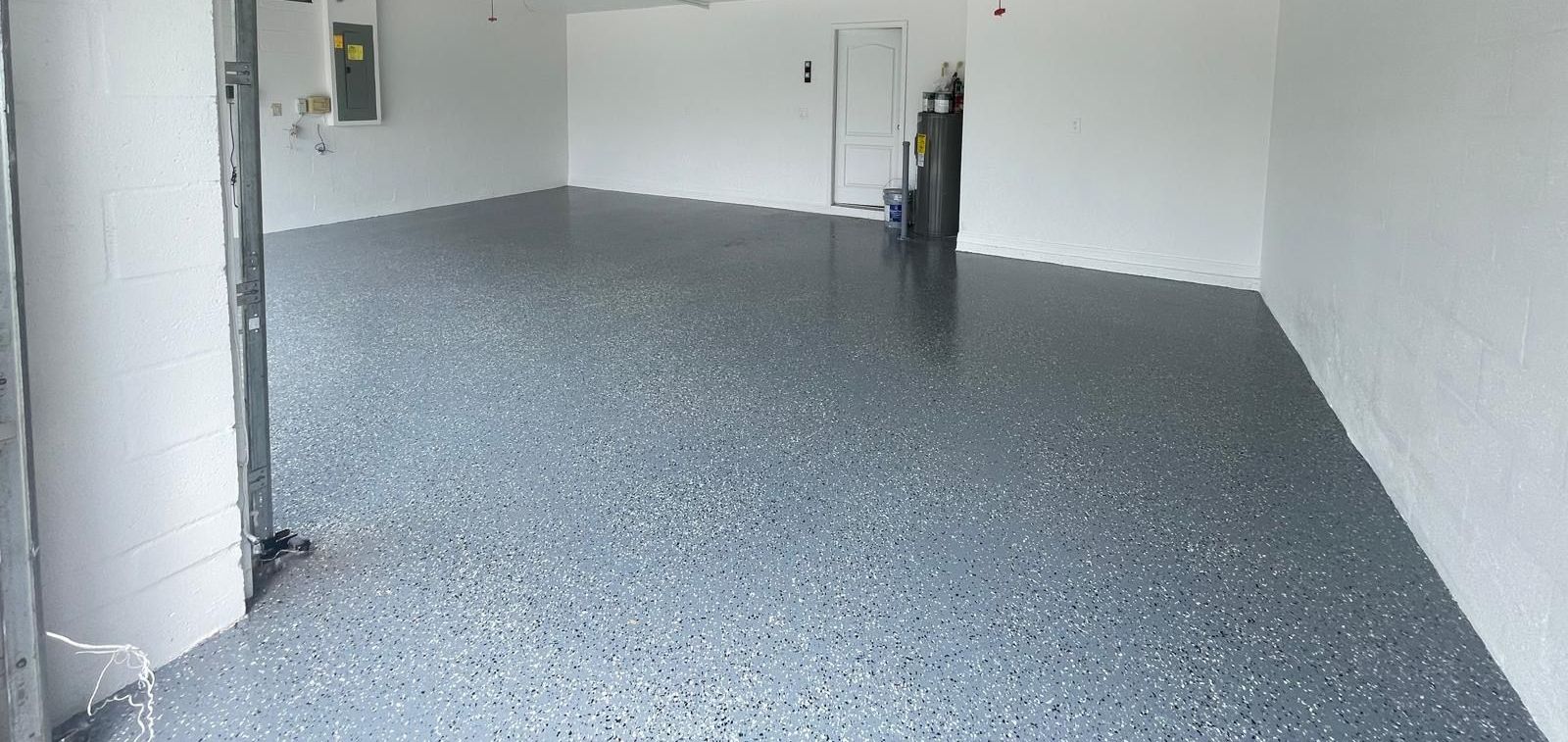 A clean, empty garage with a speckled gray epoxy floor. White walls and a partially visible door frame.