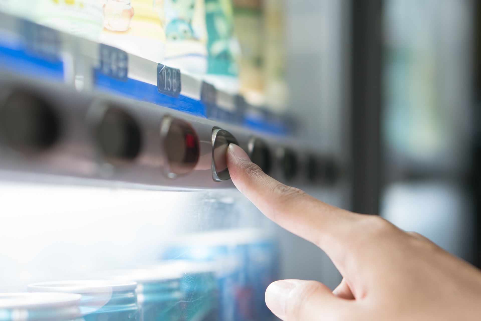 Showcasing a finger pressing a cold beverage machine button for dispensing drinks.