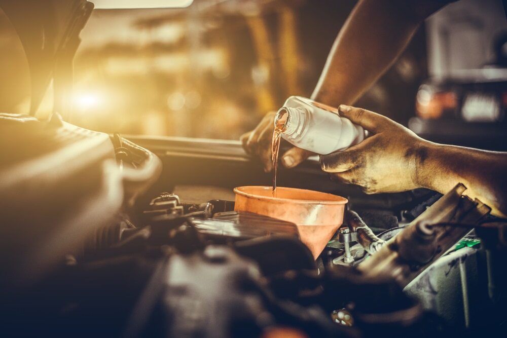 A Man is Pouring Oil Into a Car Engine — Bittkau Auto Care in Maroochydore, QLD