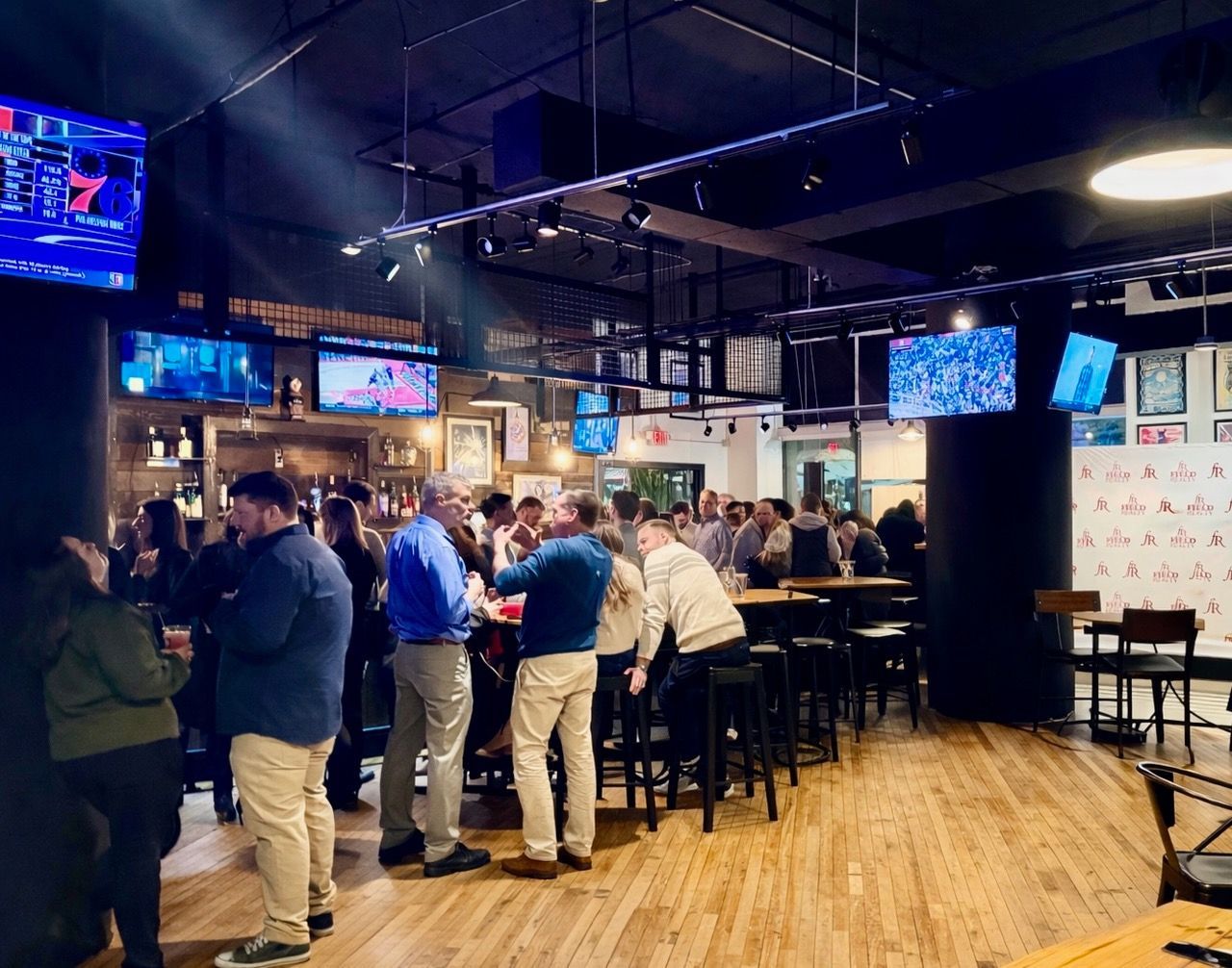 People gather inside a bar with multiple TVs on the walls; some are standing at the bar.