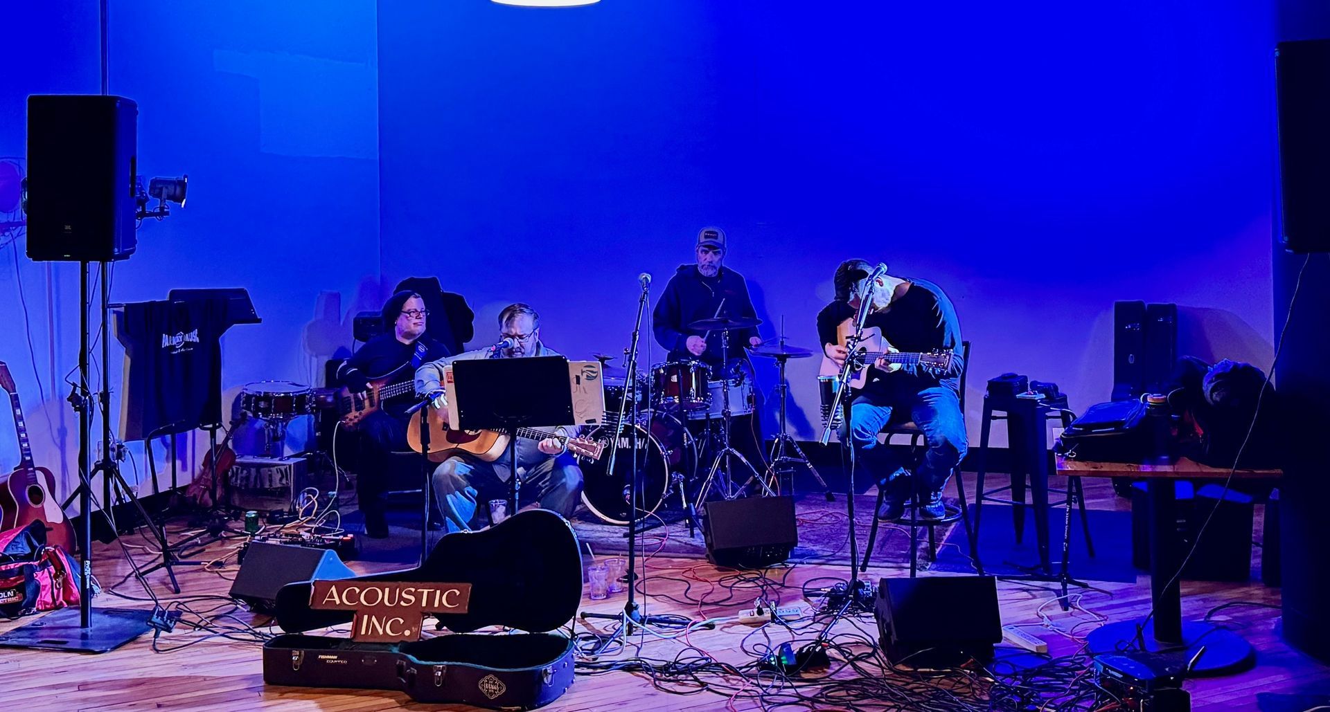 Band performing on a stage with blue lighting. Instruments include guitars, drums, and keyboards.