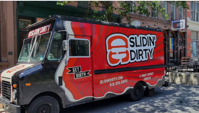 Slidin' Dirty food truck with burger logo, red and white, parked on a city street.