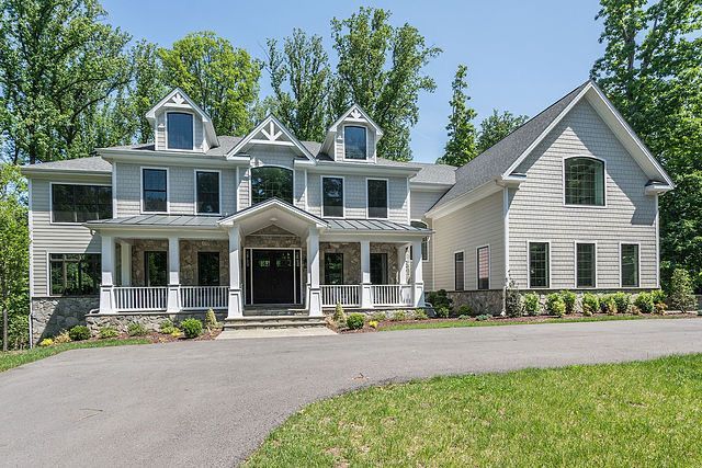 A large white house with a large porch is sitting on top of a lush green hillside.