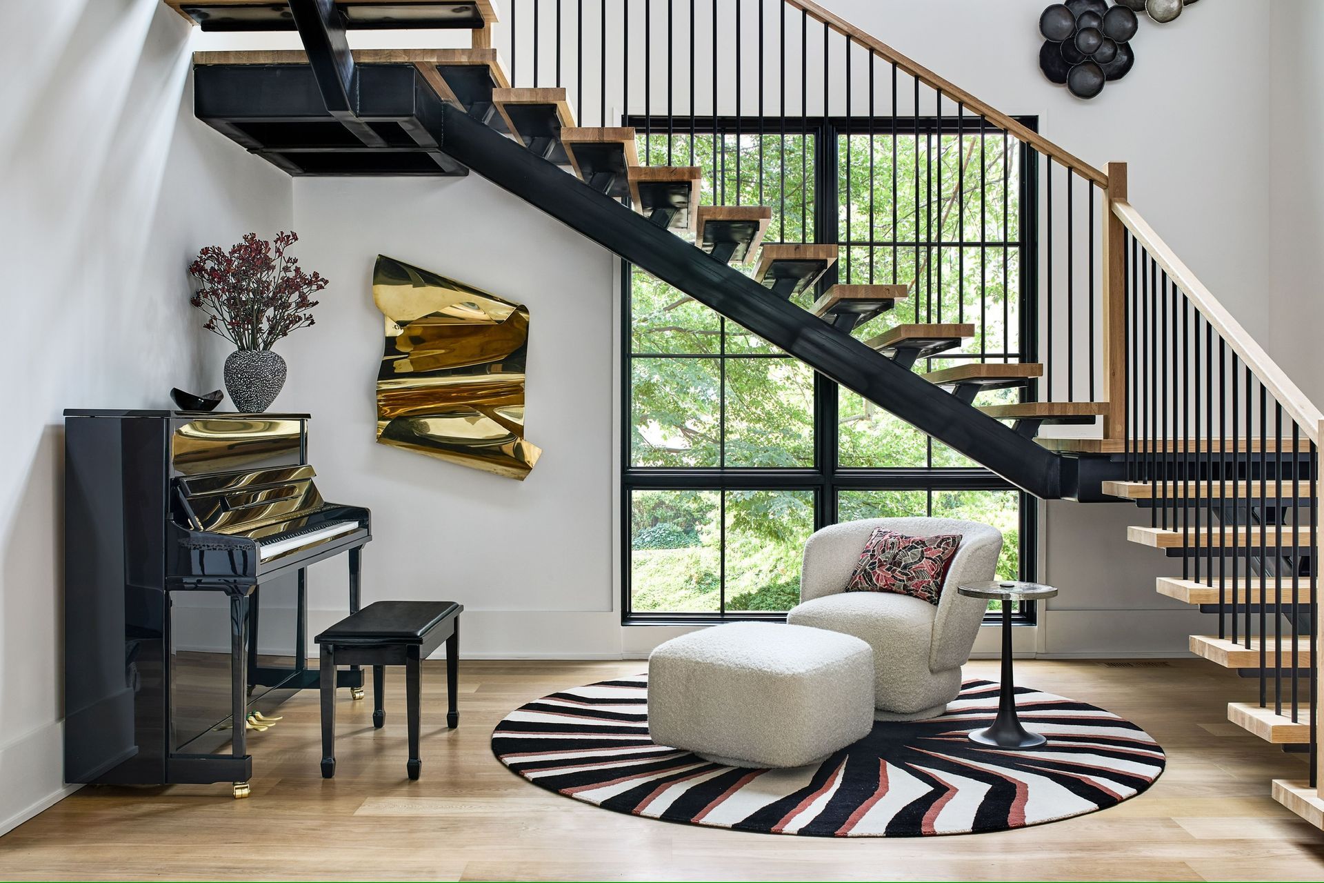 A living room with a piano , chair , ottoman and stairs.