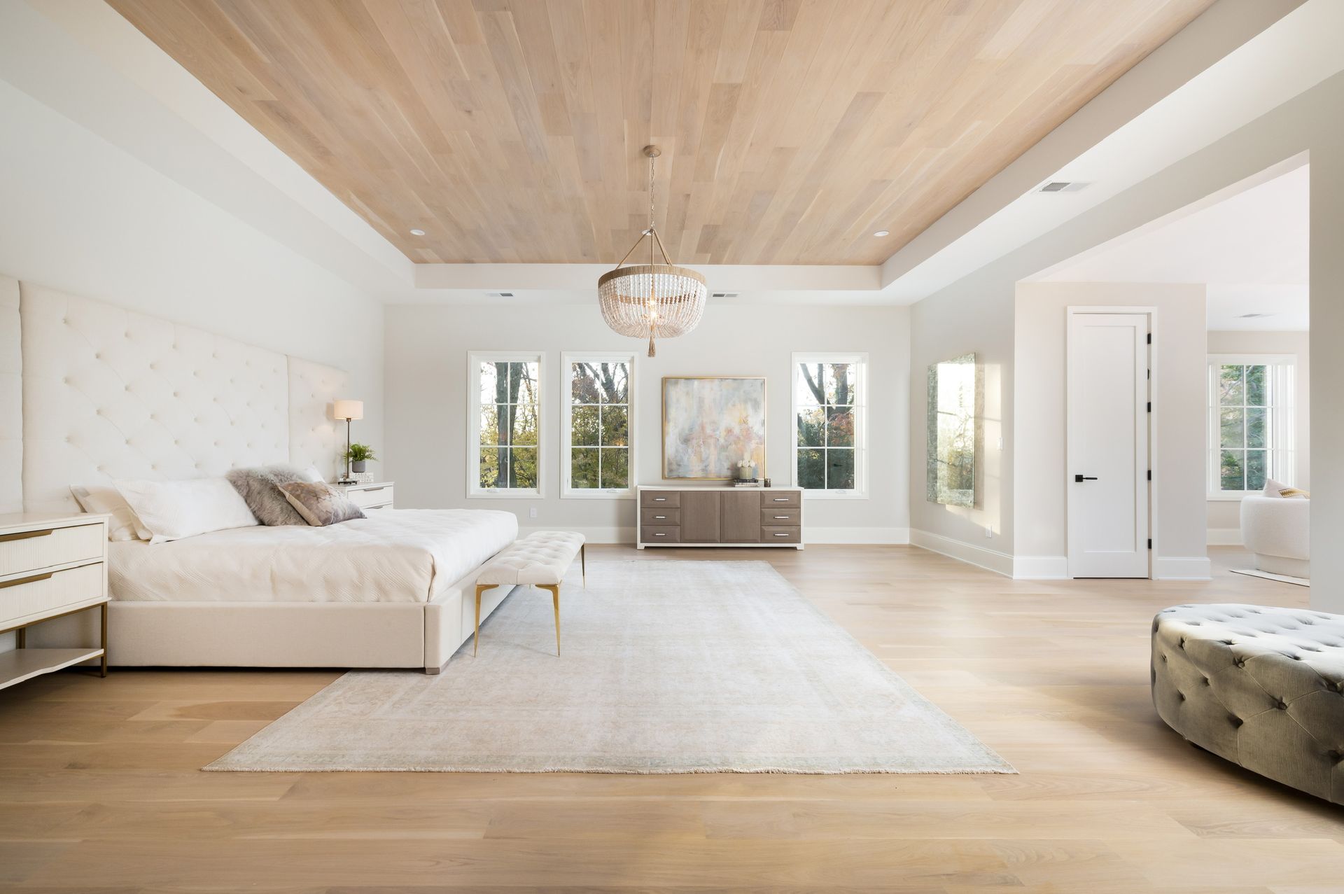 A large bedroom with a bed , ottoman , nightstand , and chandelier.