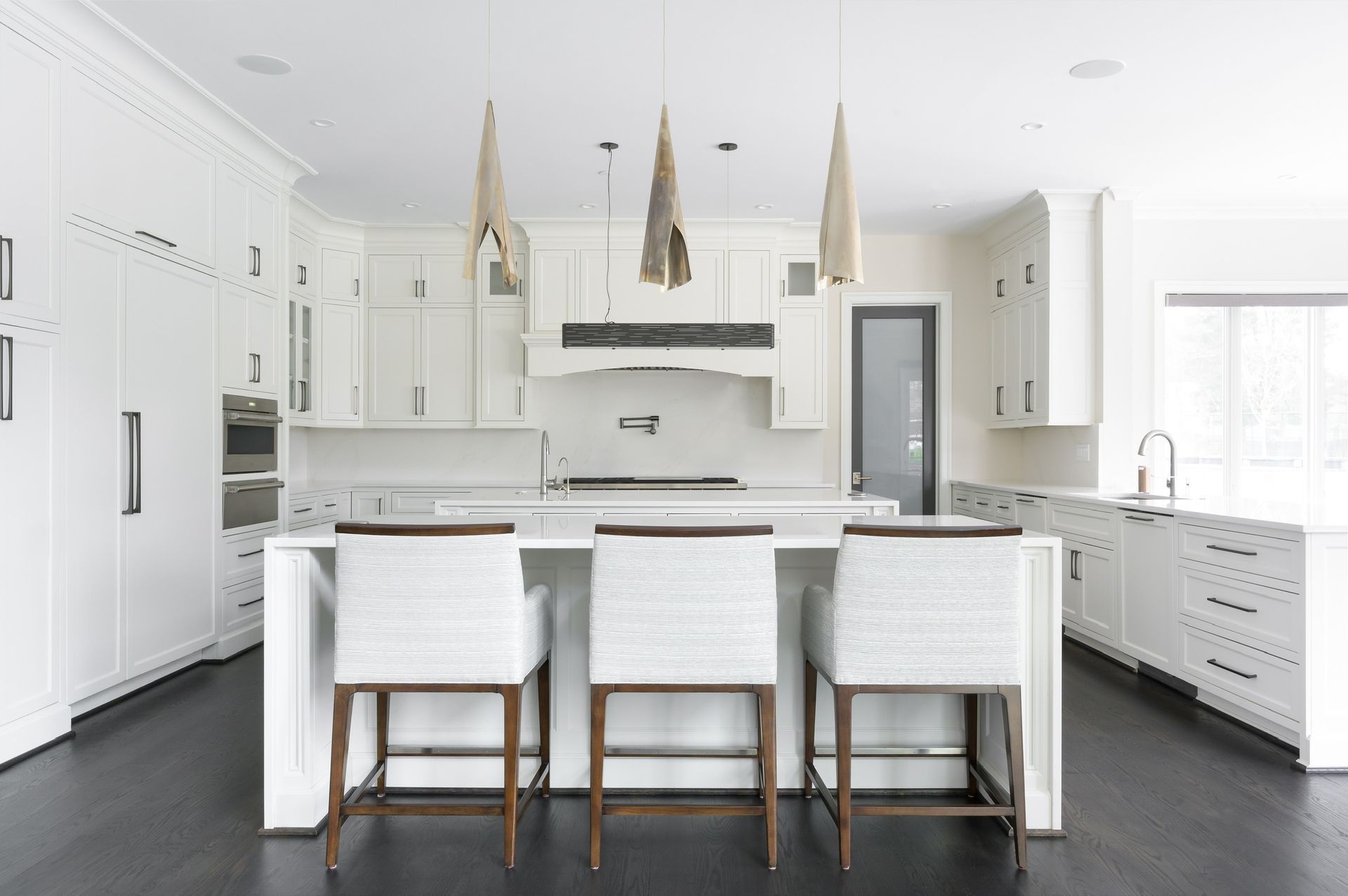 A kitchen with white cabinets and stools and a large island.