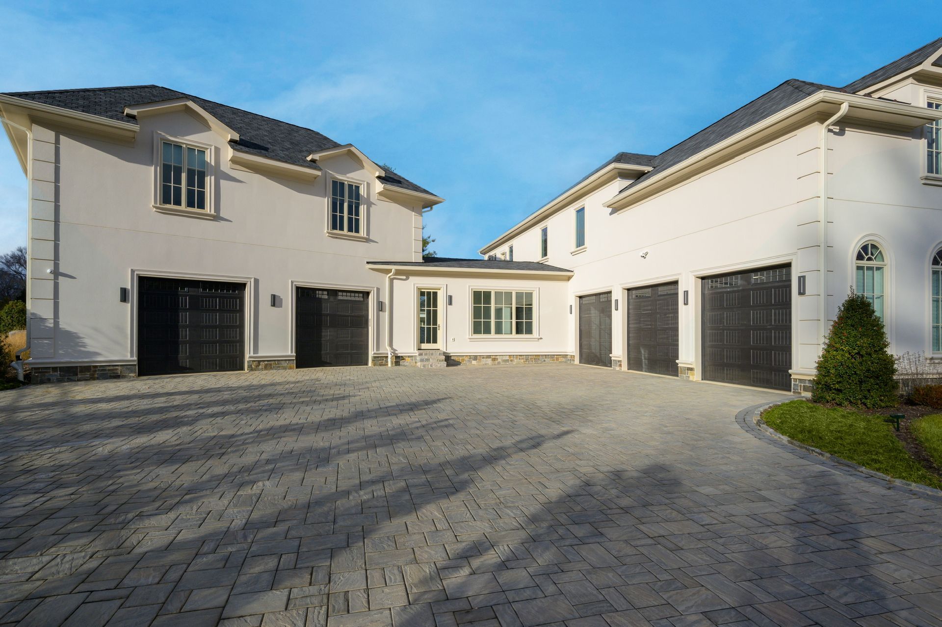 A large white house with black garage doors and a brick driveway
