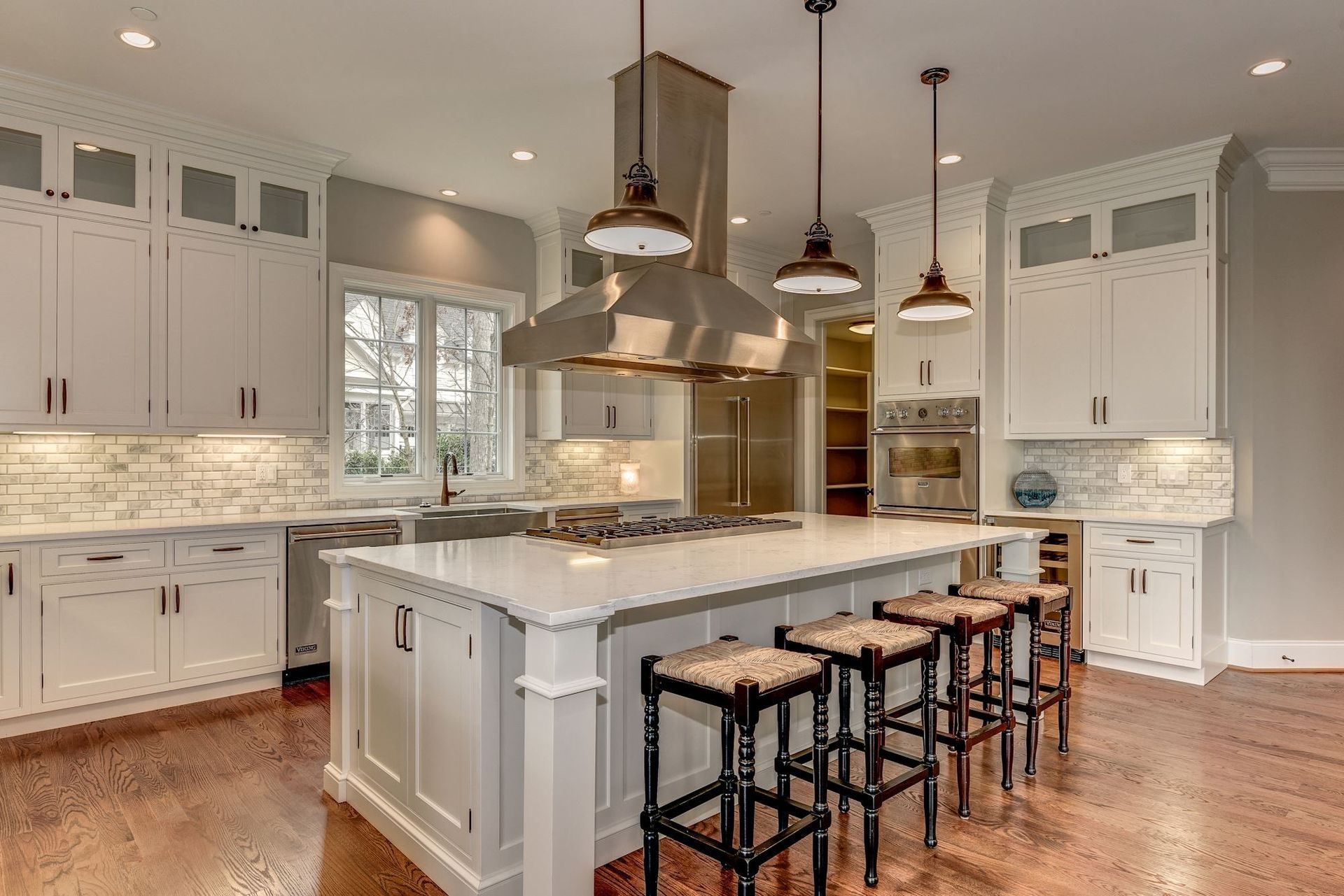 A kitchen with white cabinets , stainless steel appliances , a large island and stools.